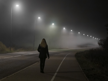 Woman walking alone on a foggy road at night, suggesting quiet danger and resolve