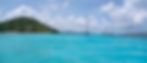 Tropical seascape with turquoise waters, anchored sailboats, and a lush green island in the background under a partly cloudy sky