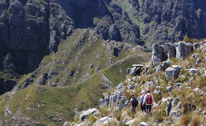 Three hikers ascend a mountain trail, overlooking a breathtaking valley below them.