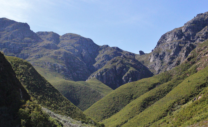 A scenic view of majestic mountains seen from a winding mountain road under a clear blue sky.