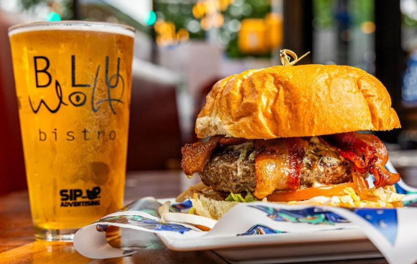 Sponsored restaurant pint glass featuring a custom logo sits on a table beside a burger at a restaurant