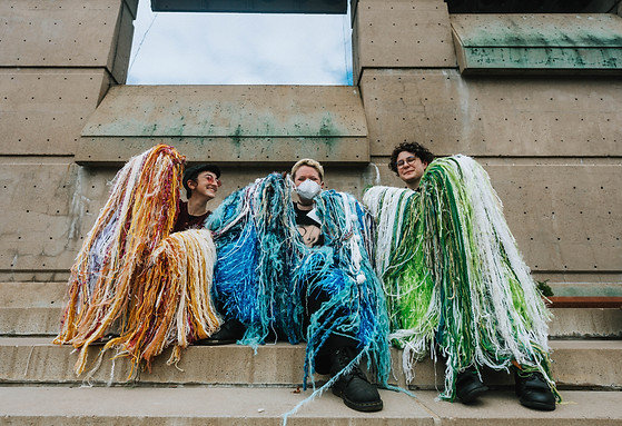 The three performers of In Touch / In Motion posing for a photo together with their flowy arms raised and seated on concrete steps
