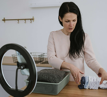Frau faltet Kleidung auf einem Tisch und erstellt dabei Content mit einem Smartphone in einem Ringlicht.