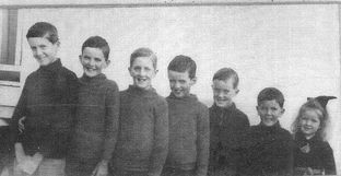 Six boys all in a row in knitted jumpers with one small girl at the end