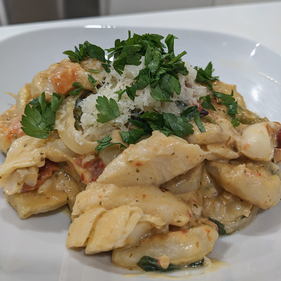 Close up of flaky pieces of white fish, fresh and sundried tomato pieces, vegetables, and pan fried gnocchi coated in a creamy sauce and topped with slightly melted parmesan cheese and fresh parsley in a white bowl.
