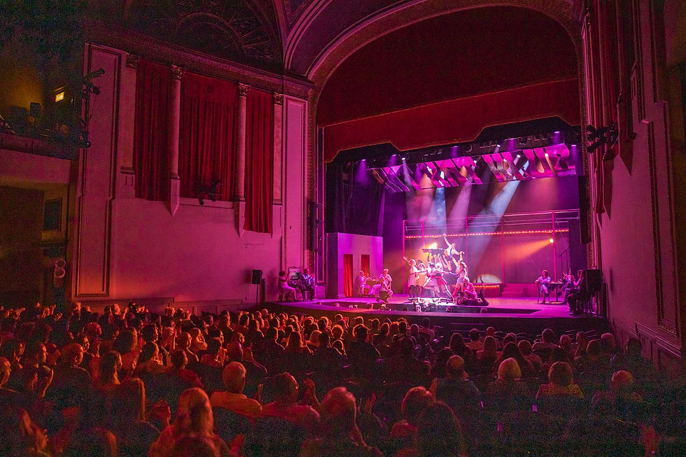 A packed audience watches a live musical performance on the brightly lit stage of the State Theatre in Uniontown, PA.