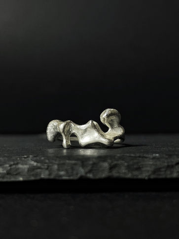 An organic, silver ring capturing the light, positioned on dark grey slate and a dark background.