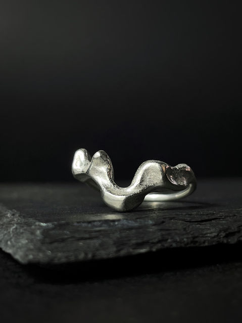 An organic, silver ring capturing the light, positioned on dark grey slate and a dark background.