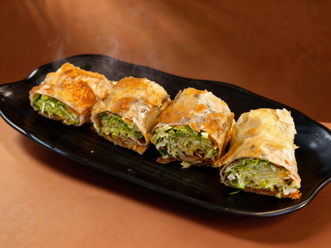 Four steaming crispy vegetable wraps on a black plate