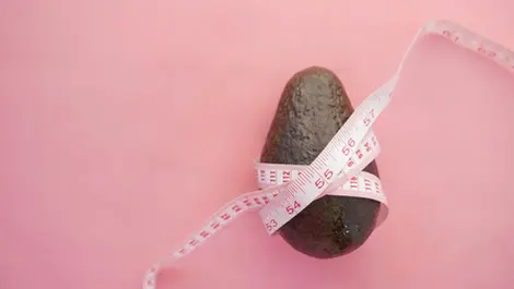 Avocado with measuring tape on pink background – symbolic image for healthy eating and weight goals with ChatGPT.