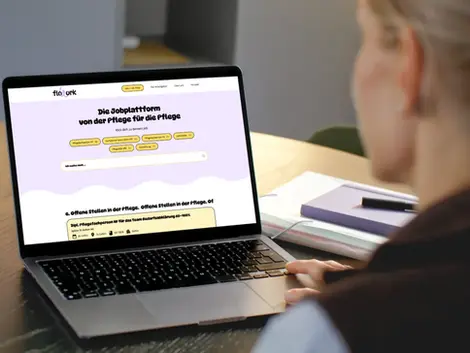 Eine Person sitzt an einem Schreibtisch und betrachtet auf einem Laptop die Startseite der Flowork Plattform, die für die Pflegebranche entwickelt wurde. Auf dem Tisch liegen Notizbuch und Arbeitsunterlagen.