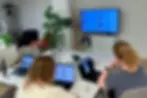 Zwei Personen aus dem Projektteam sitzen an einem Tisch, arbeiten an ihren Laptops und besprechen einen Prototyp der Flowork Plattform, der auf einem grossen Bildschirm angezeigt wird.