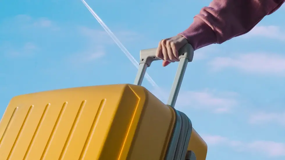 Person holding a yellow suitcase with a plane contrail visible in the background, representing international travel with a Saily eSIM