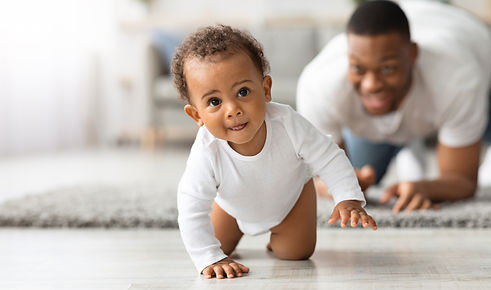 Cute Little Black Infant Baby Crawling On Floor At Home, Proud Young Father Looking At Him
