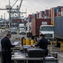 US customs officers inspect cargo documents at a major international port, with stacked shipping containers in the background.