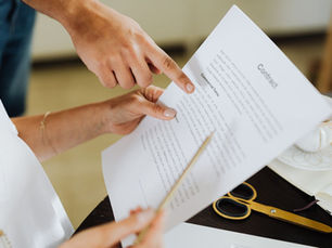 Hands review a contract document on a desk, pointing at Commercial Terms beside gold scissors and a teacup.