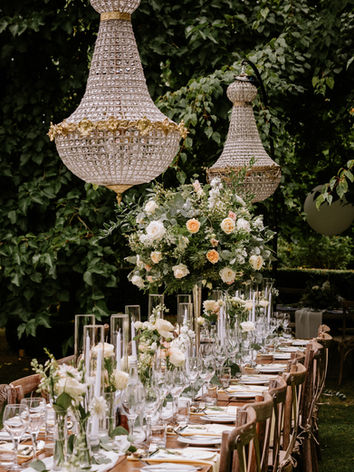 an outside wedding breakfast of long tables. with  chandeliers over the tables with white and lemon floral arrangements of candelabras and budvases of tables along the centre of the tables with tapered candles.