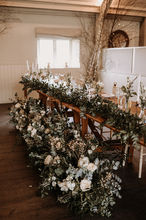 a top table at a wedding with meadow runners floral arrangements along the floor in front of the table.