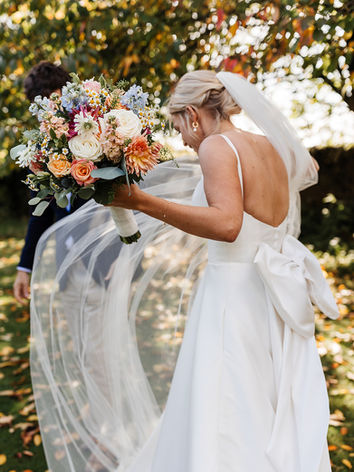 a bride with her veil catching the wind holding a bouquet of brightly coloured flowers.