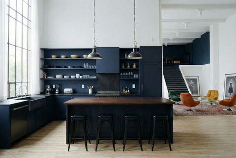 Rénovation intérieure d’un loft contemporain avec cuisine ouverte bleu nuit, îlot central en bois, étagères murales sur mesure, grandes fenêtres type verrière industrielle, parquet bois clair et escalier design, projet d’architecture intérieure à Marseille en région PACA, restructuration espace ouvert et aménagement sur mesure.