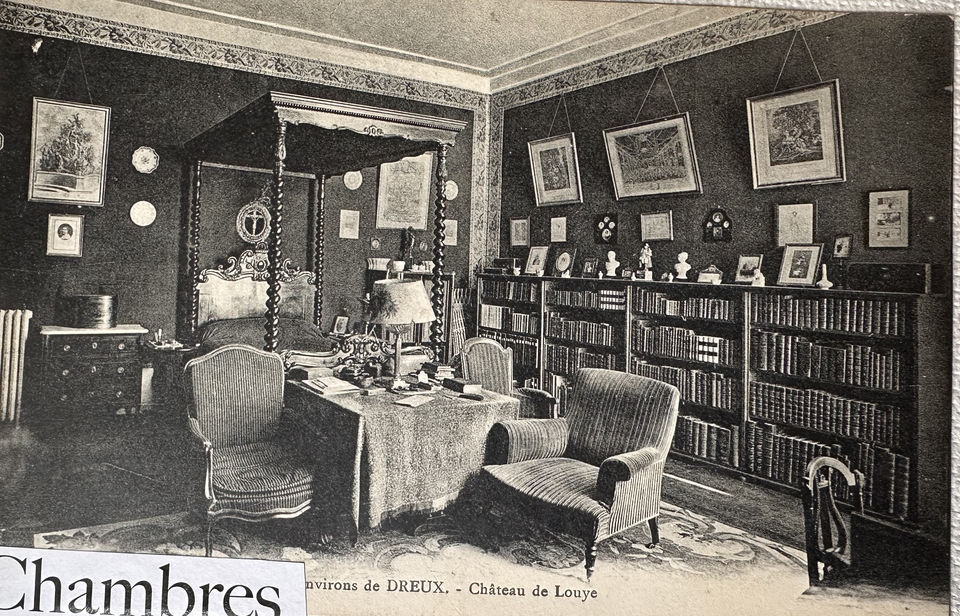 Photo ancienne en noir et blanc d'une chambre avec lit et canapé, et bibliothèque au Château de Louÿe.