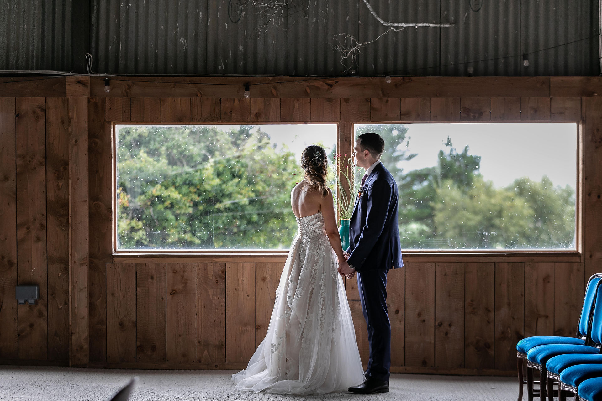 wedding couple cuddling inside barn during photoshoot looking out window