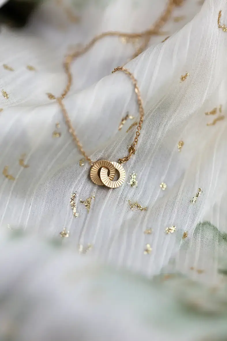 collier en acier inoxydable doré avec un petit pendentif composé de deux cercle striés entrelacés