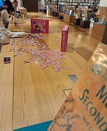People solving large puzzles inside the New York Public Library reading hall.