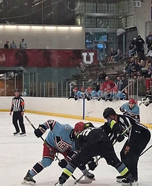 High school hockey game at Salt Lake City Sports Complex with players competing for the puck.