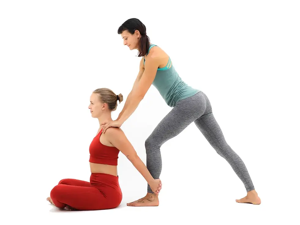 Lisa im Hands on bei einer Yogini die sich im Schneidersitz befindet, Lisa trägt eine grauen Leggins + grünes Top, Yogini in einer roten Leggins + Top