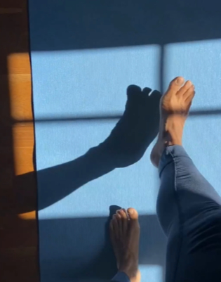 wunderschöne Yogini-Füße auf einer blauen Yogamatte vor einem mit Sonne geflutetem Fenster