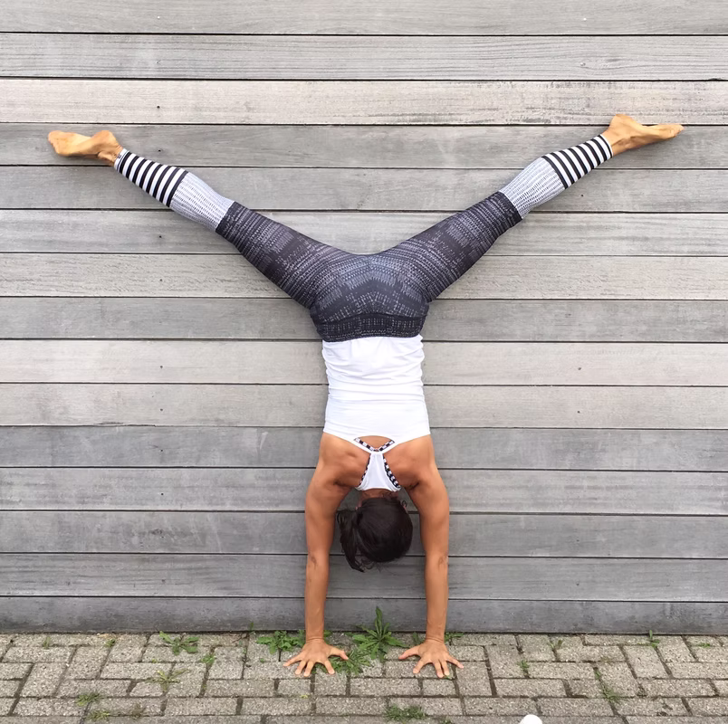 Lisa in der Yoga Asana "Handstand" vor einer Holzwand