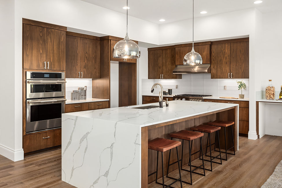 Kitchen in new luxury home with quartz waterfall island, hardwood floors, dark wood cabinets, and stainless steel appliances