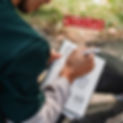 Close up of a boy writing in a notebook near the ocean. Notebook has sketches of three Boo