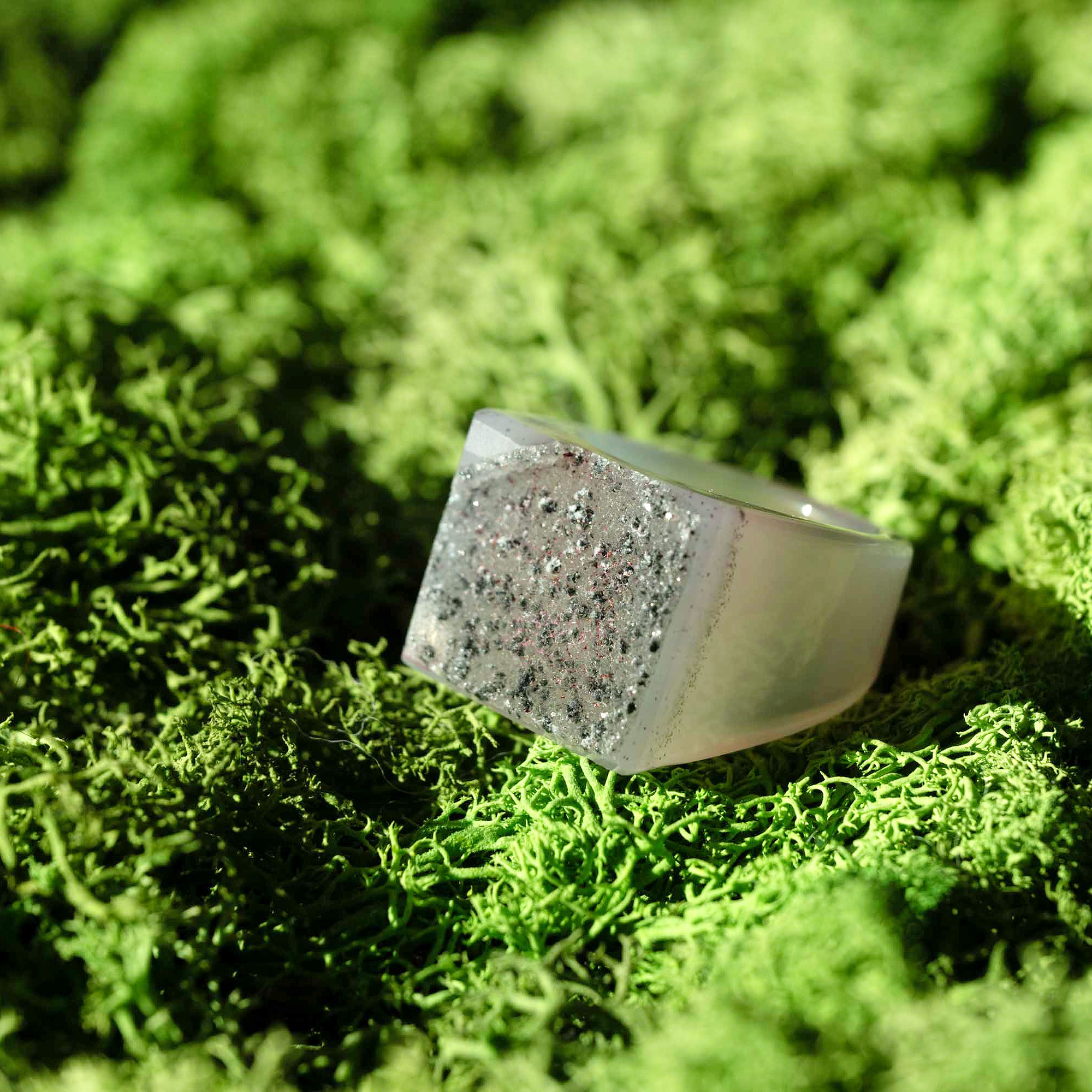 weißer Stein-Ring mit weißem Top und schwarzen Punkten auf Moosbett, Heilstein-Schmuck, alternative Methoden