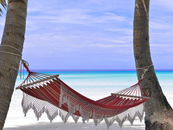 a hammock on a white sand beach facing turquoise blue water 