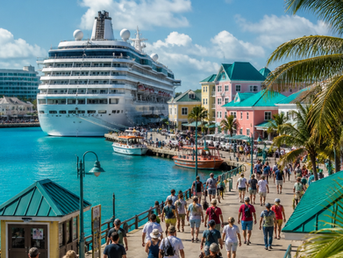 Luxury cruise ship docked in Nassau, Bahamas, with turquoise water, pastel-colored buildings, and cruise passengers walking along a sunny marina lined with palm trees and excursion boats.