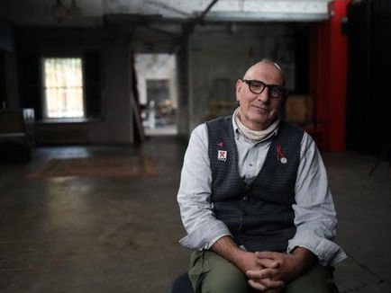Lead image: Jonathan Blake For “ Positive “ - Sky Documentary & NOW TV. Jonathan wears a white shirt and a grey knitted vest upon which there are several pins including the pink triangle and the red HIV ribbon. 