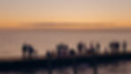 People standing on the Fire Island Pines harbor pier at sunset, looking out over the water as the sky glows with warm colors.