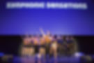 The cast of the 2016 Winnipeg Studio Theatre's production of Show CHoir! - The Musical performs "The Symphonic Sensations Super Bowl Half Time Show." The cast is dressed in gold and black costumes with their right arms pointing diagonally upwards.