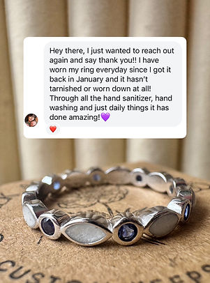 A silver ring featuring alternating marquise-shaped and round settings with white and blue stones, resting on a branded card