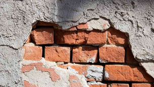 Cracked wall with exposed red bricks, rough gray plaster, and text "Brown Chimney" partially visible in lower left. Natural light.