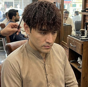 A man after his hair perming session sitting on barber chair as his barber shows his work to the camera