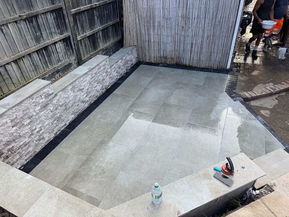Newly laid grey stone patio under construction in a fenced garden