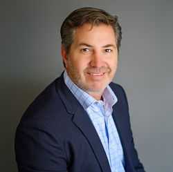 Middle-aged businessman in a navy blazer posing in a studio portrait.