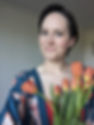 An image of the artist, Stephanie. She is a white woman with short brown hair and hazel eyes, and is holding a bunch of bright tulips.