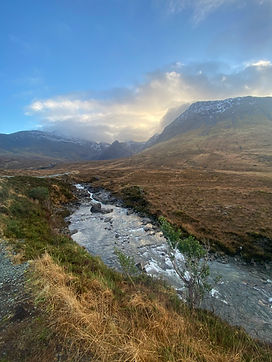 Une rivière avec des rochers au milieu des montagnes d'Ecosse sous un ciel bleu avec des nuages