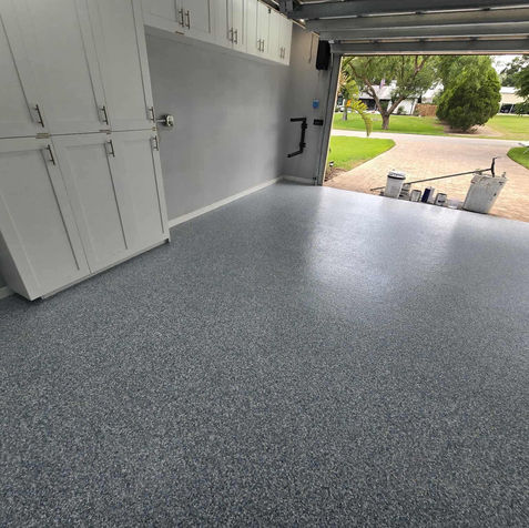 Garage interior with cabinets and storage, highlighting the calming tones of the Lagoon Blue epoxy flooring with a driveway and greenery surrounding it in the background