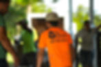 Workers stand outdoors, one in a bright orange shirt with "TRU GRIT COATINGS" and a phone number. Greenery is visible in the background.