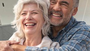 Older couple smiling and embracing in a brightly lit room, both displaying joy and warmth. Background shows a partially open garage door.
